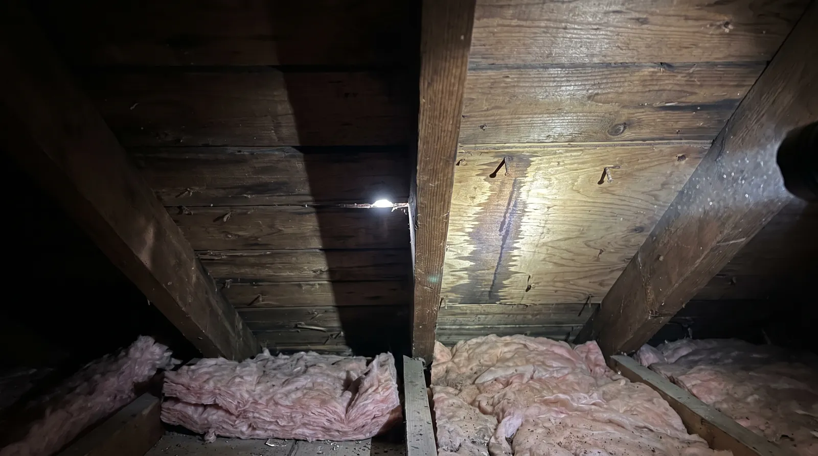 Attic view of roof decking with a daylight pinhole and water stain from a roof leak